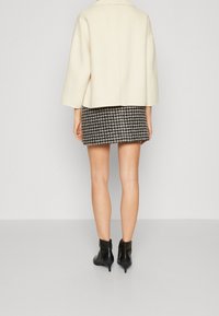 Witte, oversized jas met brede mouwen over een zwart-wit pied-de-poule minirok. Zwarte enkellaarsjes maken de outfit compleet.