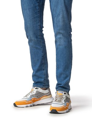 Sportssko i grå, orange og hvid med en tekstureret overdel, polstret krave og tyk sål, kombineret med blå jeans.
