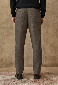 Gray wool trousers with a textured surface, featuring a straight cut, two back pockets, and a slim fit. Worn with dark shoes.