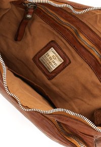 Interno di una borsa in pelle marrone con una fodera in tessuto beige, dotata di una cerniera argento, una tasca con cerniera e un'etichetta impressa sulla pelle.