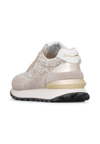 Sneaker da donna con tomaia beige testurizzata, dettagli in pelle liscia, colletto imbottito e branding dorato. Suola intermedia bianca e suola esterna in gomma nera.