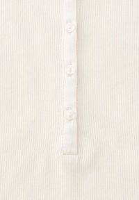 Close-up van witte ribbelstof met een verticale strook waarop drie kleine witte knopen zijn genaaid.