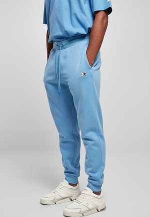 Hellblaue Jogginghose mit elastischem Bund und Kordelzug, ausgestattet mit seitlichen Taschen und einem kleinen schwarzen Logo am Oberschenkel.