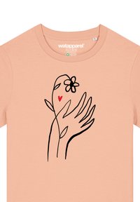 T-shirt couleur pêche avec un dessin à ligne noir de deux mains tenant une fleur et un accent de cœur rouge, présentant un col rond.
