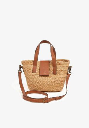 Bolso de paja trenzada con asas de cuero marrón y correa ajustable. Presenta un logo grabado en un parche de cuero. Forma compacta y redonda.