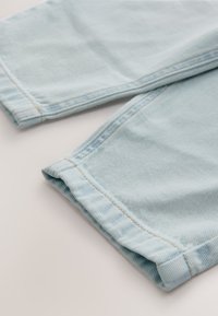 Tissu en denim bleu clair avec une texture côtelée, présentant des revers roulés et des coutures contrastées. Design simple et décontracté.