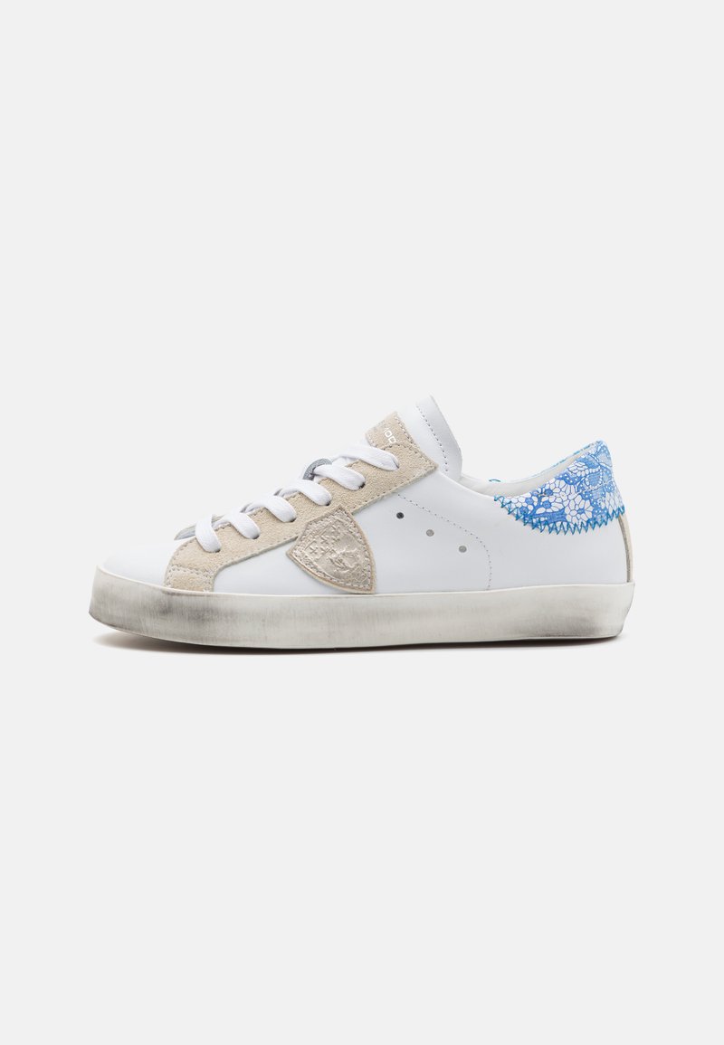 Hvite sneakers med beige semsket skinn detaljer, snøring ved hælen, rund tå og gummisåle. Minimalistisk design med perforerte sider.