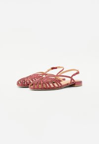 Rote gewebte Sandalen mit flacher Sohle, offener Zehenpartie und verstellbarem Knöchelriemen; verfügen über eine geflochtene Textur und einen minimalistischen Stil.