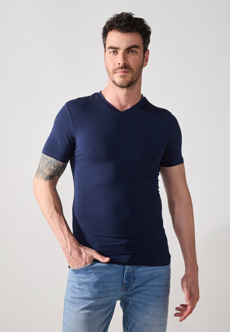 Marineblå kortermet V-hals t-skjorte laget av mykt stoff, designet for en tettsittende silhuett, kombinert med lyseblå jeans.