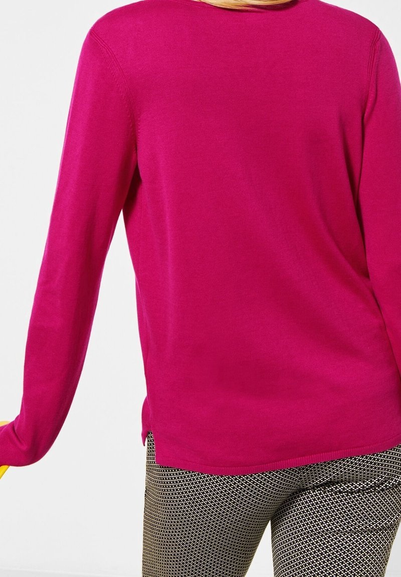 Personne portant un haut à manches longues rose vif et un pantalon à motifs noir et blanc, vue de dos à partir de la taille.