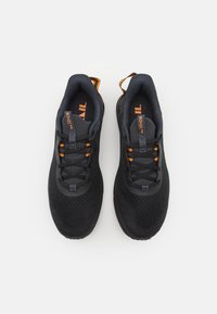 Chaussures de sport noires avec une tige en mesh, des accents orange et des lacets noirs. Elles présentent un col rembourré et une semelle texturée pour une meilleure adhérence.
