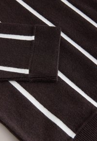 Brun tröja med breda vita ränder. Ribbstickade muddar och halsringning med mjuk stickad textur, vilket skapar en lager-på-lager-effekt.