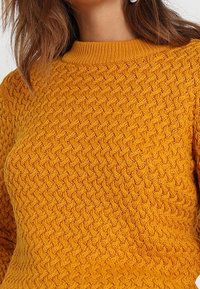 Sweter dziergany w żywym musztardowym kolorze, z teksturowanym wzorem, okrągłym dekoltem i prążkowanymi mankietami dla dopasowania.