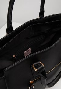Sac à main noir texturé avec deux poignées, détails de fermeture éclair dorés et compartiment principal ouvert montrant une poche intérieure zippée avec une étiquette de marque.