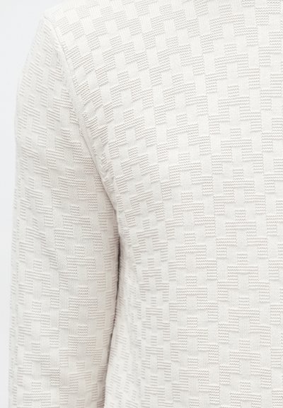 Tissu crème texturé avec un motif géométrique composé de carrés en relief. Le design est subtil, avec une texture douce en maille sur la surface.