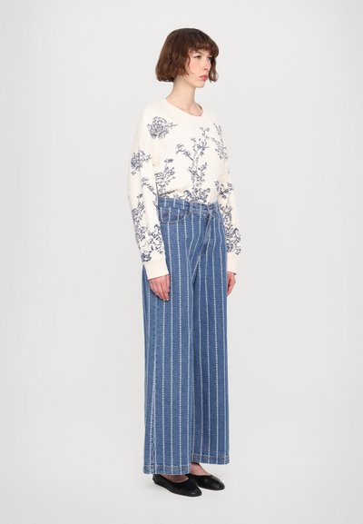 Cream sweater with navy floral print, paired with high-waisted blue wide-leg jeans featuring vertical white stripes. Black shoes.