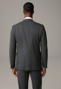 Ciemnoszara marynarka w eleganckim fasonie, wykonana z fakturowanej tkaniny, z jednym rozcięciem, dwoma bocznymi kieszeniami oraz kontrastowymi białymi detalami kołnierza.