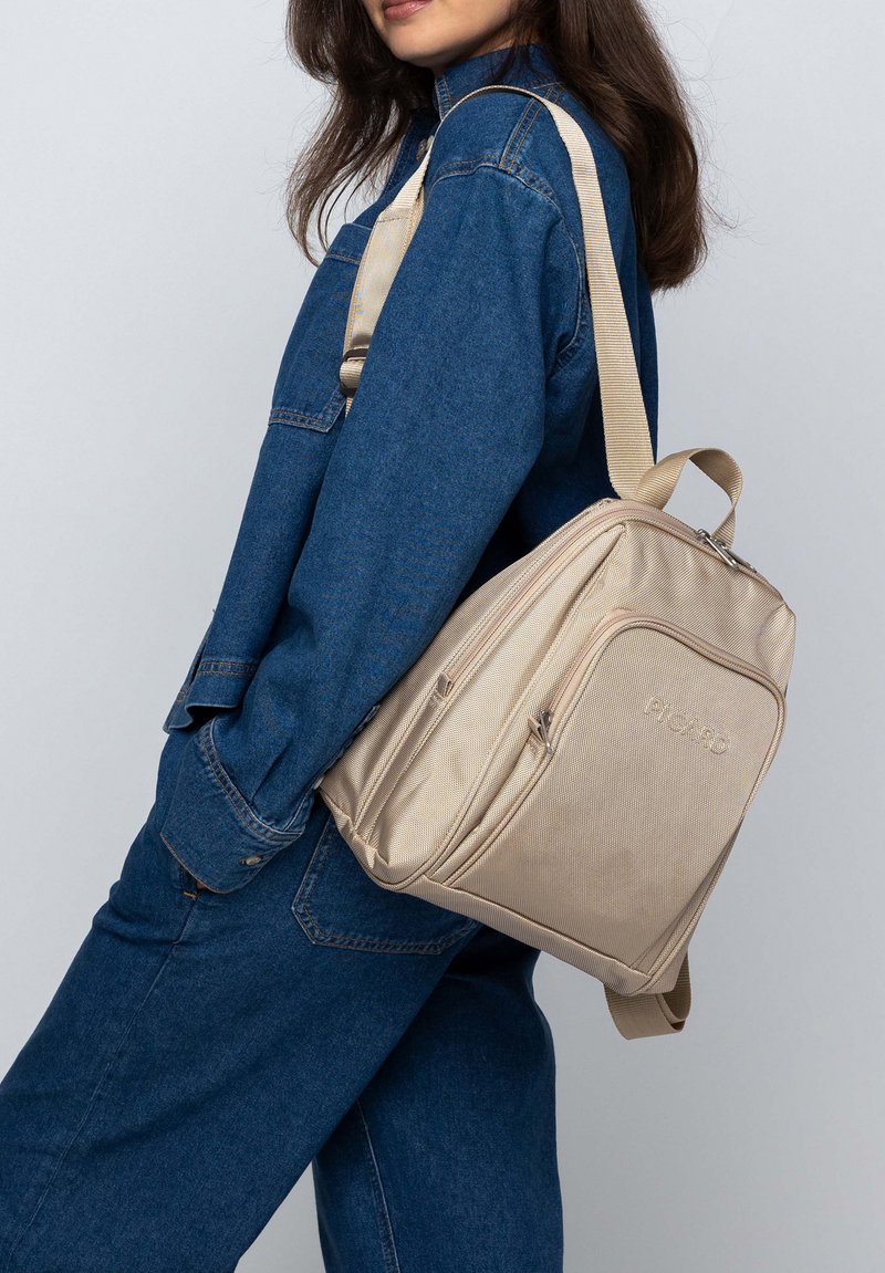 Zaino in nylon beige con superficie testurizzata, dotato di più scomparti con cerniera, tracolla regolabile e design elegante e angolare.