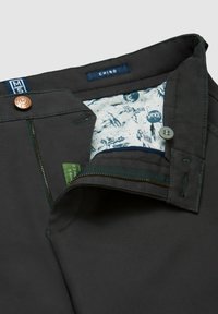 Gray chino pants featuring a copper button, zipper closure, and patterned inner lining with green tag detailing.