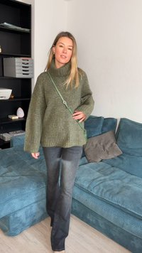 Olive green oversized sweater with ribbed hem, paired with dark gray flared jeans. Displays a textured knit design and a crossbody bag.