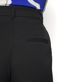 Pantalon noir sur mesure avec une texture lisse, un devant plat et une seule poche arrière avec un détail discret de couture.