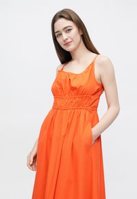 Oranžové šaty bez rukávov so zladeným pásom. Hladká látka a splývavá sukňa. Disponujú bočnými vreckami a štvorcovým výstrihom.