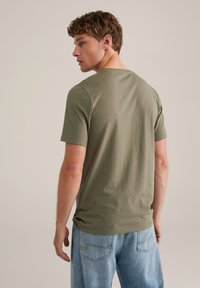 Camiseta de manga corta en verde oliva, con cuello redondo, textura suave, diseño ajustado, combinada con jeans de denim azul claro.
