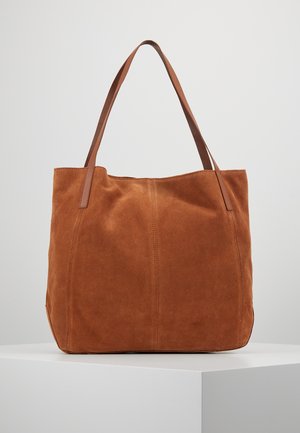 Brown suede tote bag with two long leather shoulder straps, standing upright on a white pedestal against a plain light background.