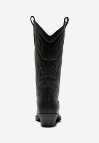 Botas de vaquero de cuero negro con punta puntiaguda y patrones de costura elevados. Cuentan con lengüetas para facilitar el uso y un diseño de tacón bajo.