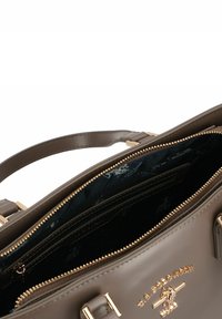 Bolso sintético marrón con herrajes en tono dorado, compartimentos con cremallera y un interior oscuro con patrón. Cuenta con dos asas para llevar.