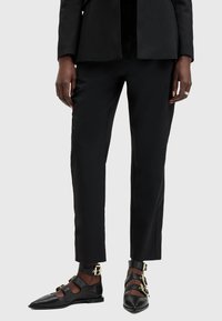 Svarta skräddarsydda byxor med slim fit och slät yta, kombinerade med svarta platta skor med remmar och detaljer i guld.