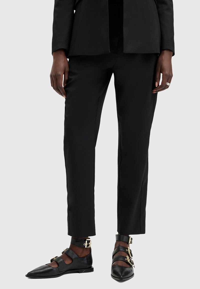Svarta skräddarsydda byxor med slim fit och slät yta, kombinerade med svarta platta skor med remmar och detaljer i guld.
