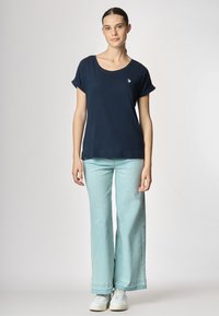 T-shirt blu navy a maniche corte con scollatura rotonda, caratterizzato da un piccolo logo sul petto e una vestibilità comoda, abbinato a jeans a gamba larga in azzurro chiaro.