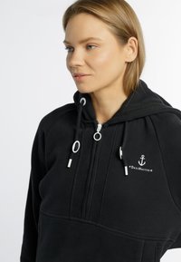 Zwarte hoodie gemaakt van zachte stof, voorzien van een rits, witte touwtjes en een ankerlogo met de geborduurde tekst "DreiMaster".
