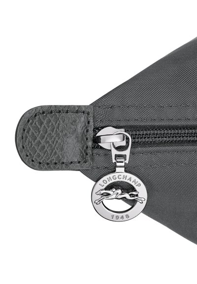 Black fabric pouch corner with a zipper featuring a round silver Longchamp logo pull tab showing a horse and rider.