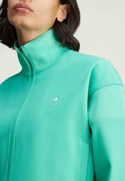 Giacca verde con zip realizzata in morbido tessuto, dotata di un alto collo, un logo discreto sul petto e tasche laterali.