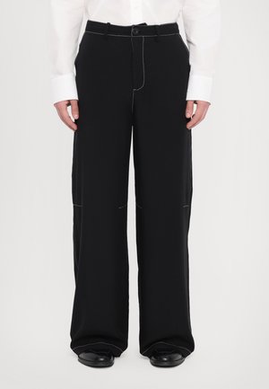 Schwarze weite Hose aus glatter Stoffqualität, mit weißen Nähten, einem Knopfverschluss und seitlichen Taschen.