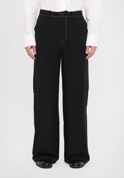 Pantalones de pierna ancha negros, fabricados en tejido suave, con detalles de costura blanca, cierre de botón y bolsillos laterales.