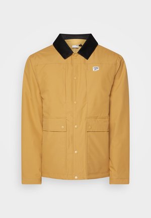 Giacca gialla impermeabile con colletto in velluto a coste nero, bottoni a pressione visibili e due tasche frontali. Presenta un piccolo logo Puma.