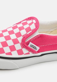 Baskets Vans slip-on avec un motif en damier rose et blanc, dessus en toile, accents élastiques sur les côtés et semelle en caoutchouc noir.