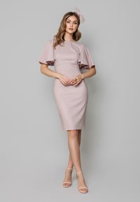 Pudrowo różowa sukienka z bufkami, dopasowany fason, długość do kolan, fakturowany materiał. Połączona z cielistymi sandałkami na paski, minimalna biżuteria.