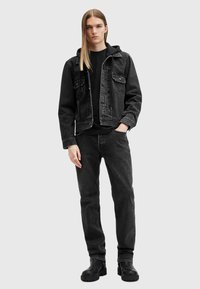 Sort denimjakke med brystlommer, parret med en sort hættetrøje, sorte jeans og sorte støvler; glat tekstur, afslappet pasform.