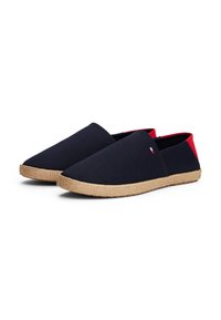 Navy blauwe canvas instappers met een rode hielaccent en juten touwzool. Glad textuur, minimalistisch design en ronde neusvorm.