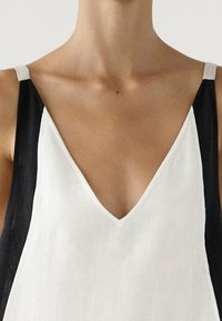 Selsiddet top med en dyb V-halsudskæring, lavet af hvidt og sort stof med kontrasterende stropper. Glat tekstur, minimalistisk design.
