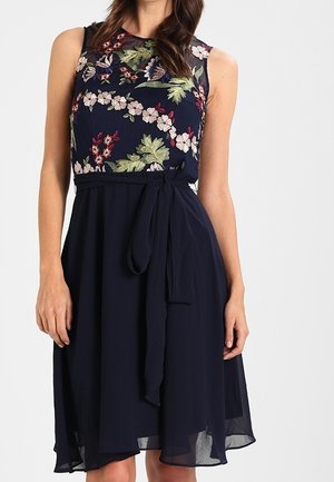 Tmavě modré šaty s květinovou výšivkou na živůtku, bez rukávů a s vázáním v pase. Vyrobené z lehké, splývavé látky.