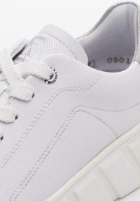 Baskets blanches avec une tige en cuir texturé, bout rond, lacets blancs, accents argentés sur la languette et une épaisse semelle en caoutchouc à motif.