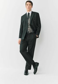 Czarny garnitur szyty na miarę z podwójnie zapinaną marynarką, wzorzystą kamizelką, białą koszulą, cz Tie i wypolerowanymi czarnymi butami. Gładka struktura tkaniny.