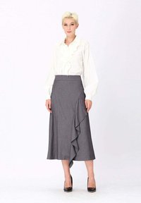 Blouse blanche à volants avec des manches longues et une jupe portefeuille à rayures grises avec un ourlet en volants, associée à des escarpins noirs.