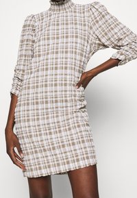 Brown and white checkered dress with a high neck, long sleeves, and side ruching detail, made of textured fabric.