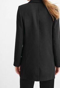 Sort skræddersyet frakke med en lige silhuet, klapkrave og lange ærmer. Glat stof med rygslids og minimalistisk design.